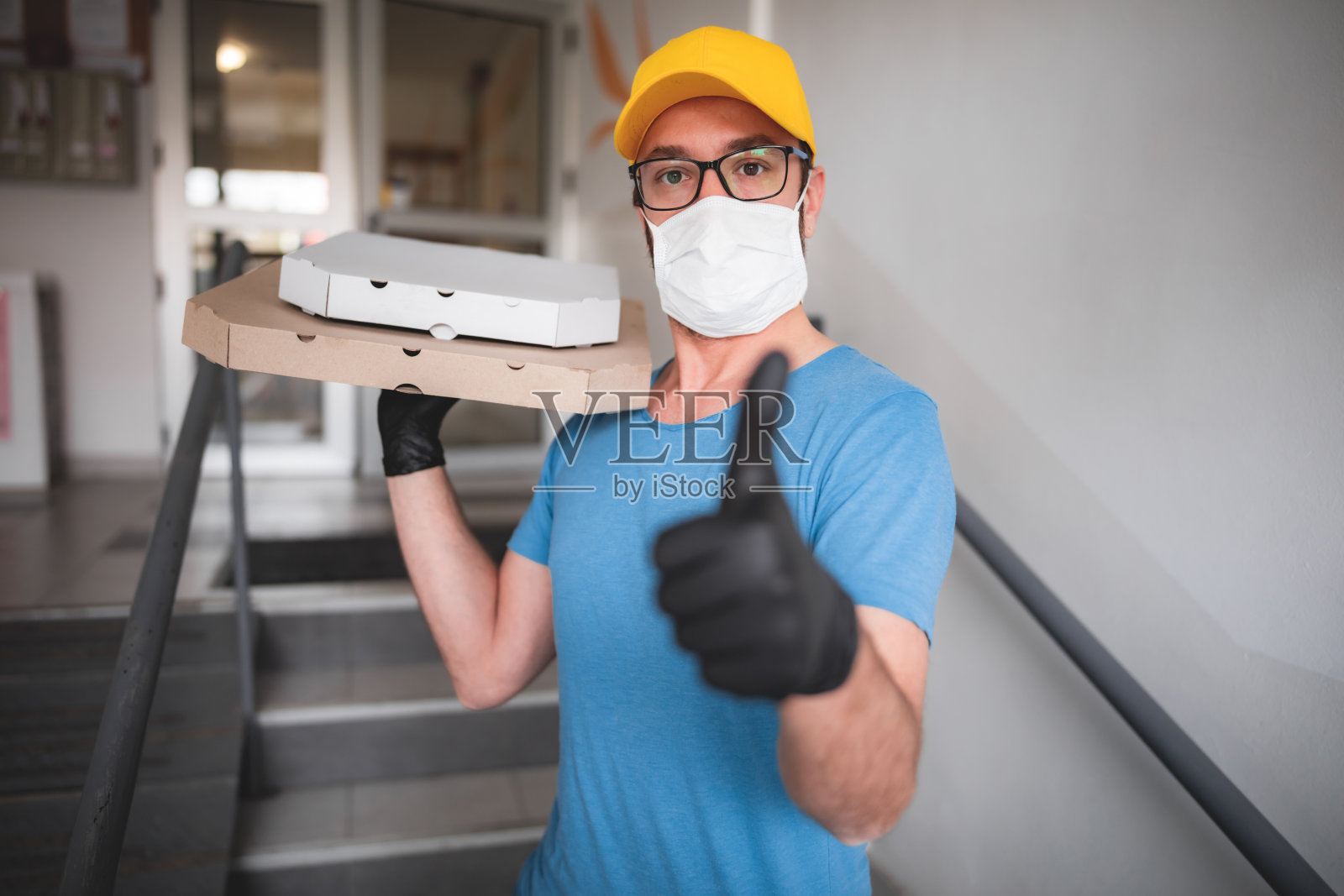 送餐员带着医用防护口罩拿着披萨盒-病毒和大流行的日子，送餐上门。照片摄影图片