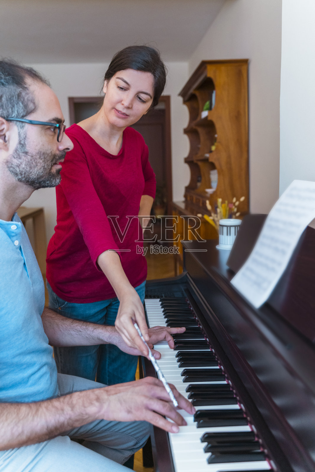 垂直视图的钢琴课在家里。女教师向中年男学生讲解一堂音乐课。照片摄影图片