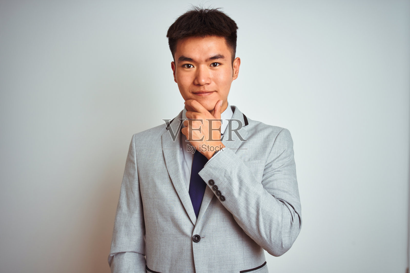 穿着西装打领带的亚洲华人商人站在孤立的黄色背景下，双臂交叉，手举下巴，微笑着看着镜头，看起来很自信。积极的思考。照片摄影图片