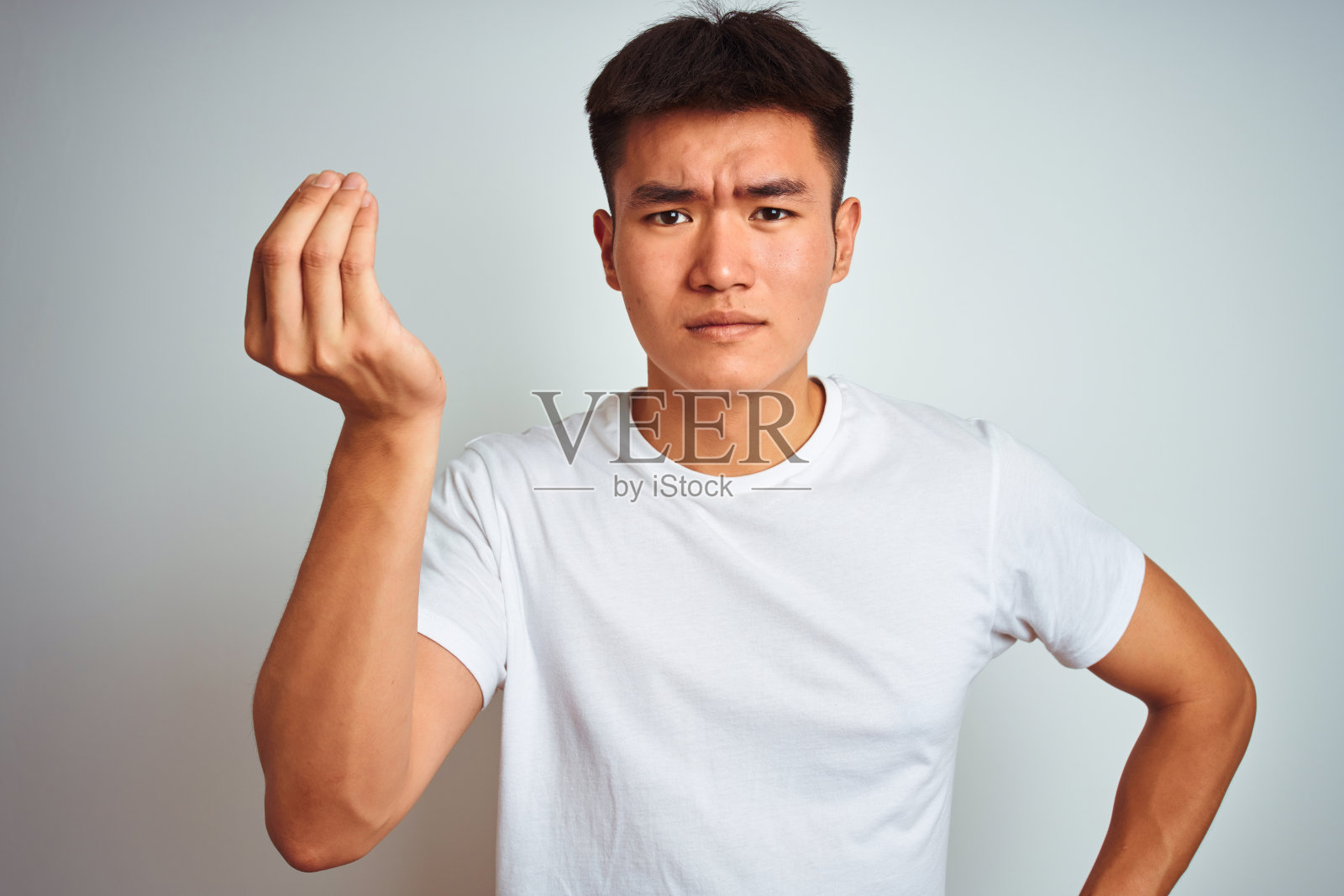 年轻的亚洲华人男子穿着t恤站在孤立的白色背景做意大利手势的手和手指自信的表情照片摄影图片