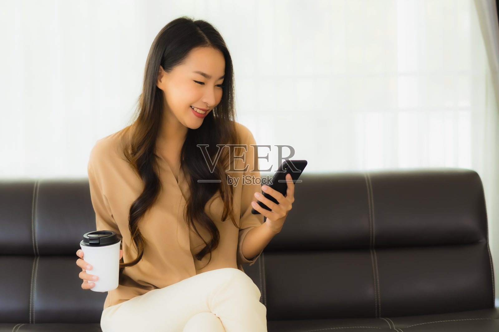 描绘美丽的年轻亚洲女性在客厅沙发上使用手机或手机和咖啡杯照片摄影图片