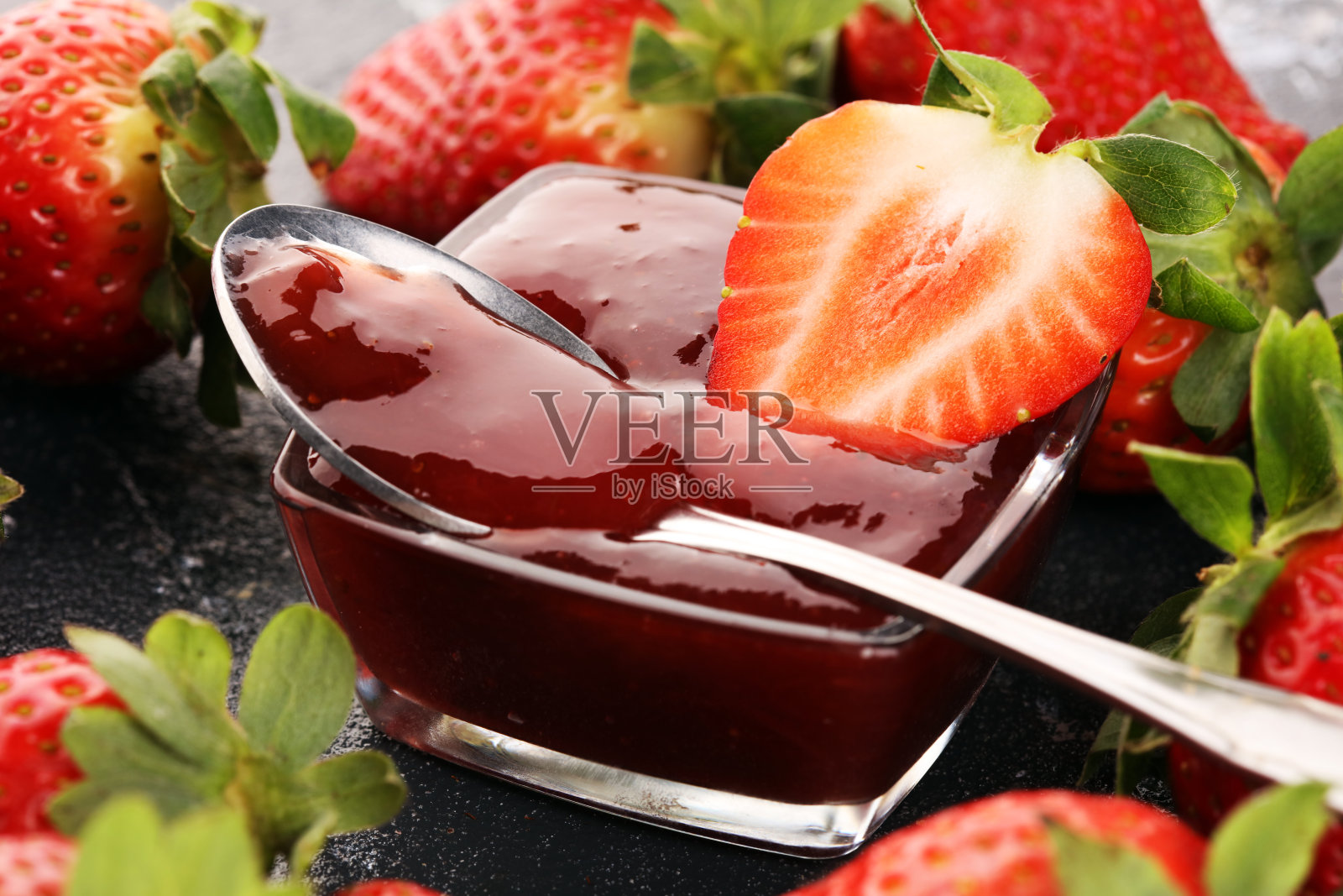 草莓酱在玻璃罐中，草莓和树叶在乡村的背景。自制草莓果酱或果酱照片摄影图片