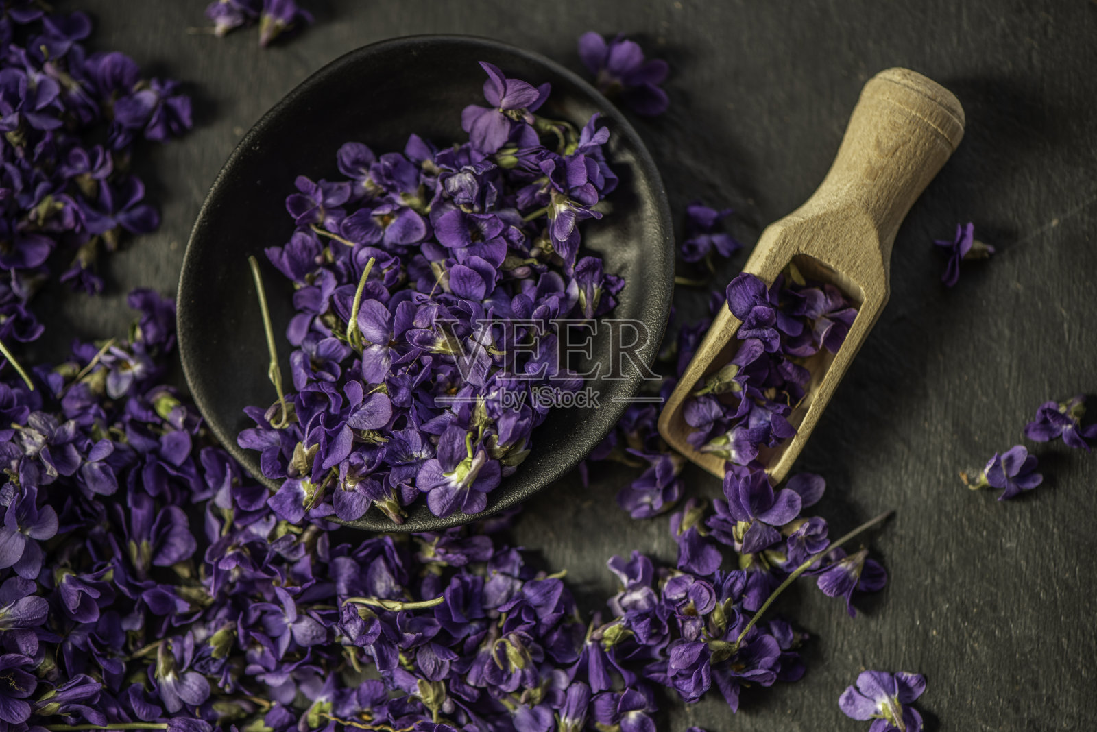 新鲜紫罗兰紫罗兰花头在一个黑色陶瓷盘子与木勺照片摄影图片