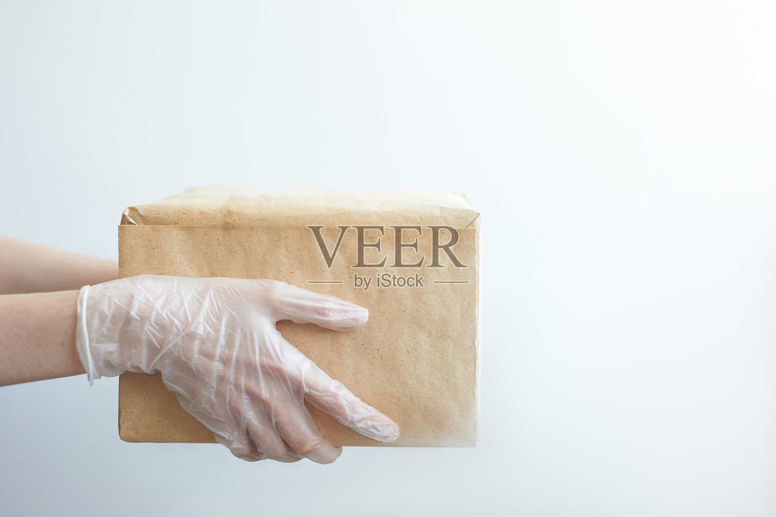 带医用手套的快递员给顾客一个包裹。隔离中的交付服务。新冠肺炎大流行的影响。快递员拿着一个纸板箱在白色背景下照片摄影图片