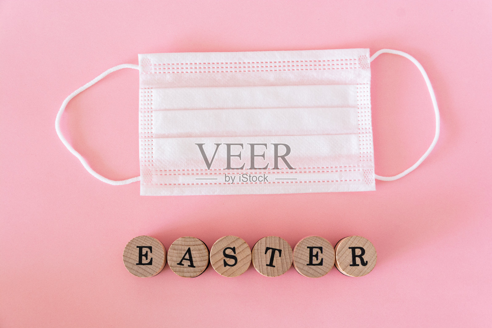 平躺着，木制的字母写着复活节，粉色的背景上有防护面具照片摄影图片