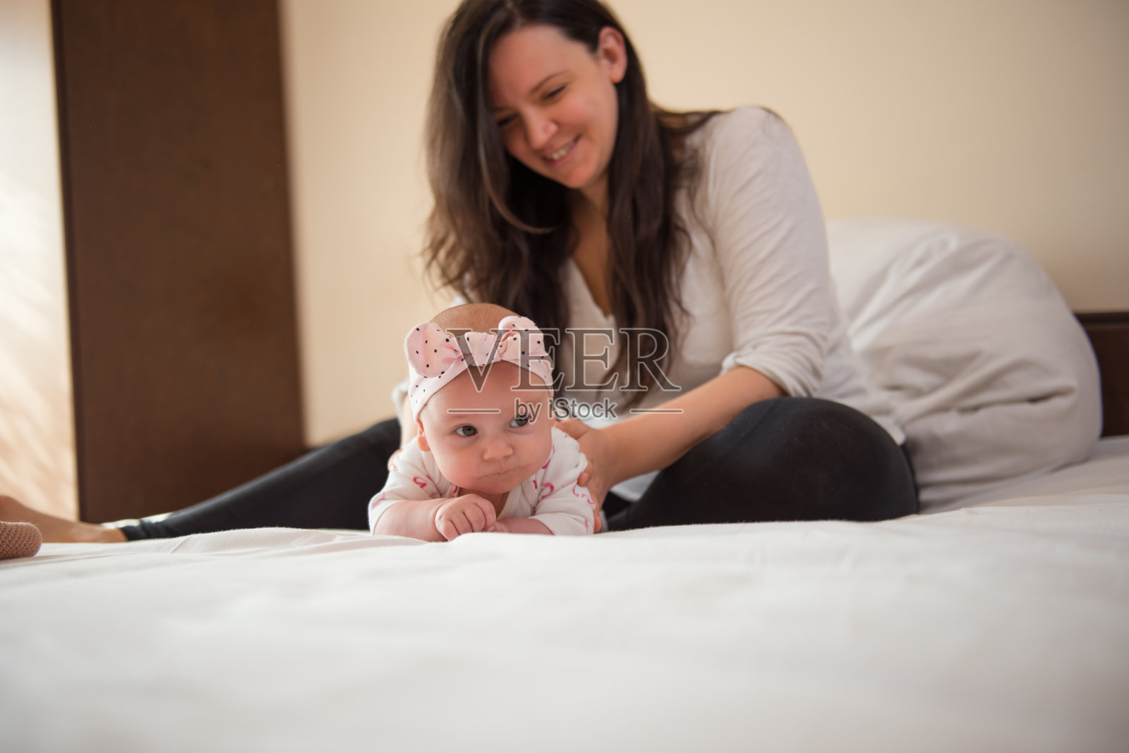 可爱的小女孩在床上爬，背景是她的妈妈照片摄影图片