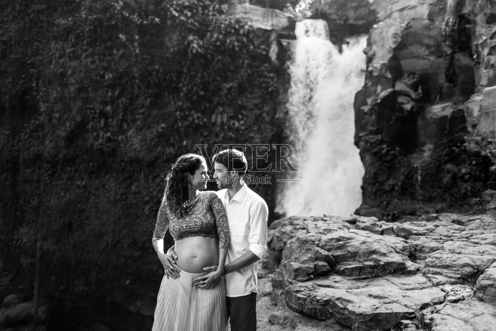 年轻的孕妇夫妇喜欢Tegenungan瀑布的美景，沐浴在晨光中，幸福地在一起，享受怀孕旅行生活照片摄影图片