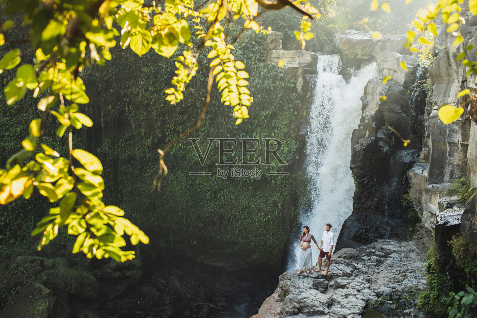 年轻的孕妇夫妇喜欢Tegenungan瀑布的美景，沐浴在晨光中，幸福地在一起，享受怀孕旅行生活照片摄影图片