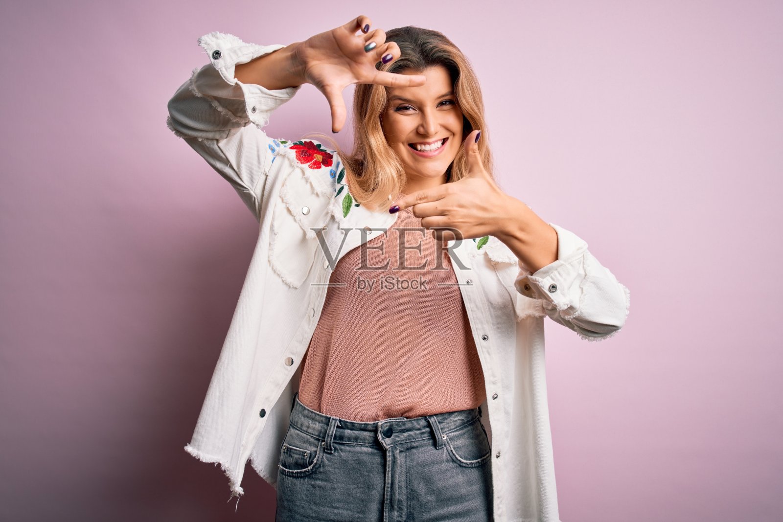 年轻美丽的金发女人穿着休闲夹克站在孤立的粉红色背景微笑与手和手指框架与快乐的脸。创意和摄影概念。照片摄影图片
