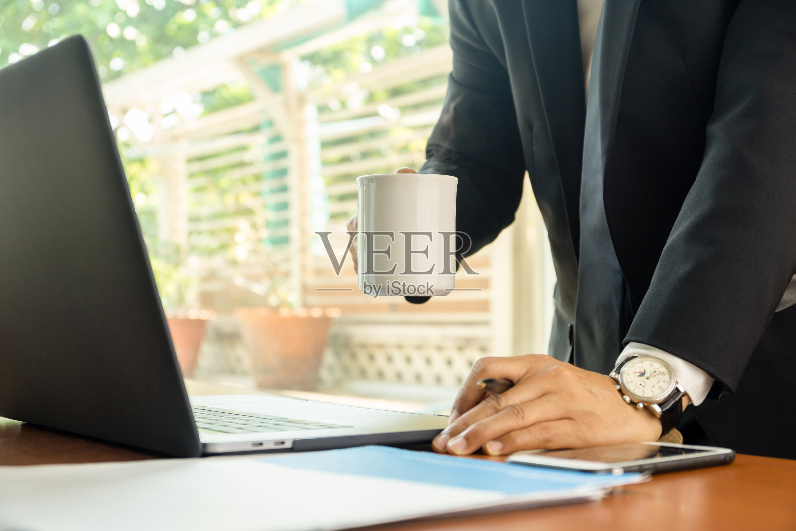 商人拿着咖啡杯，桌上有笔记本电脑照片摄影图片