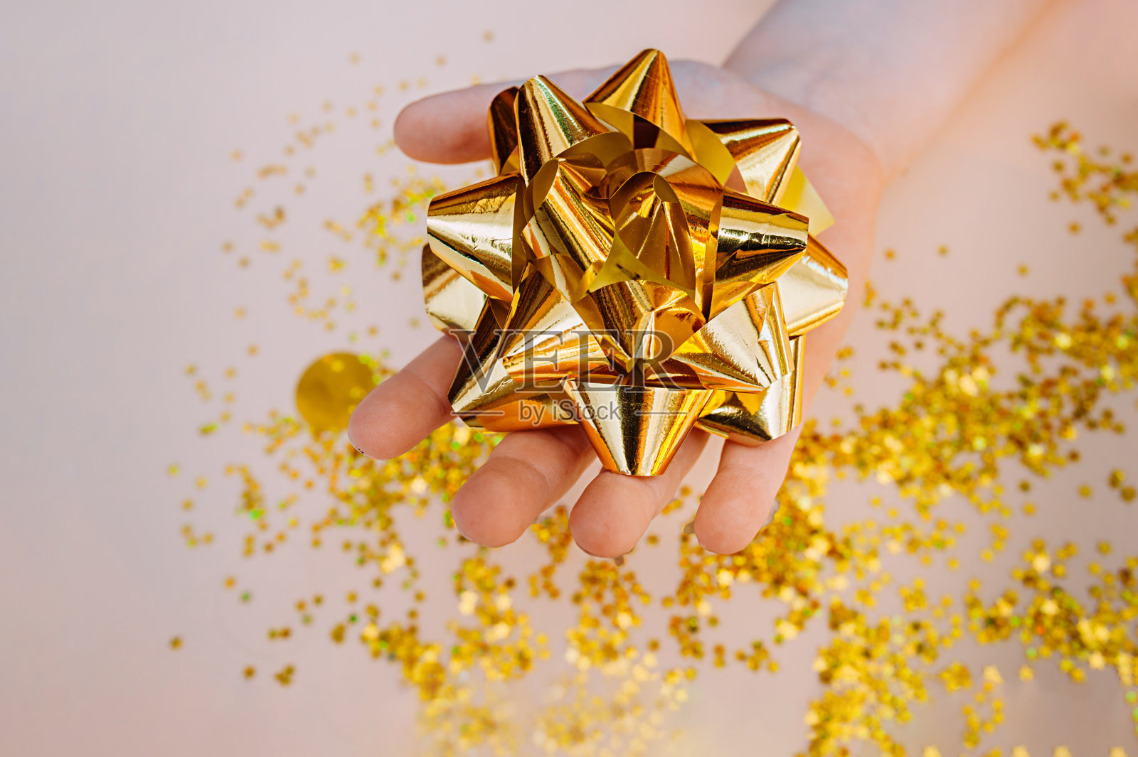 浅色皮肤的手握一个大的金箔弓，背景是在一个柔和的米色背景上分散的金色星星。照片摄影图片