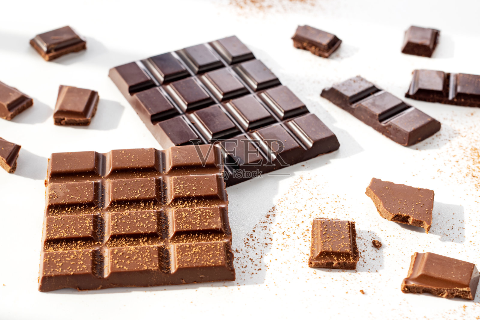 黑色和牛奶巧克力与可可粉散布在白色的背景照片摄影图片