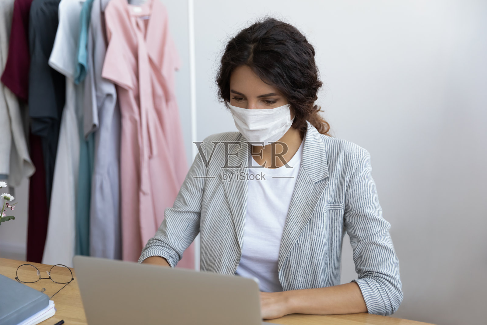 健康的年轻女商人戴着面具在办公室用电脑工作。照片摄影图片