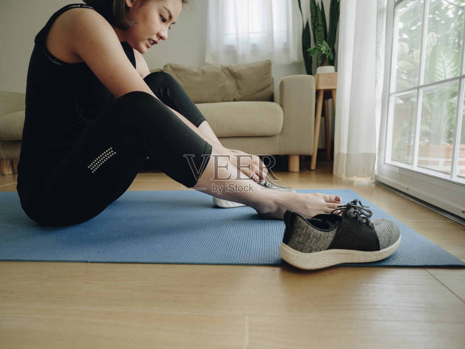 在家里的客厅里系鞋带的亚洲妇女。照片摄影图片