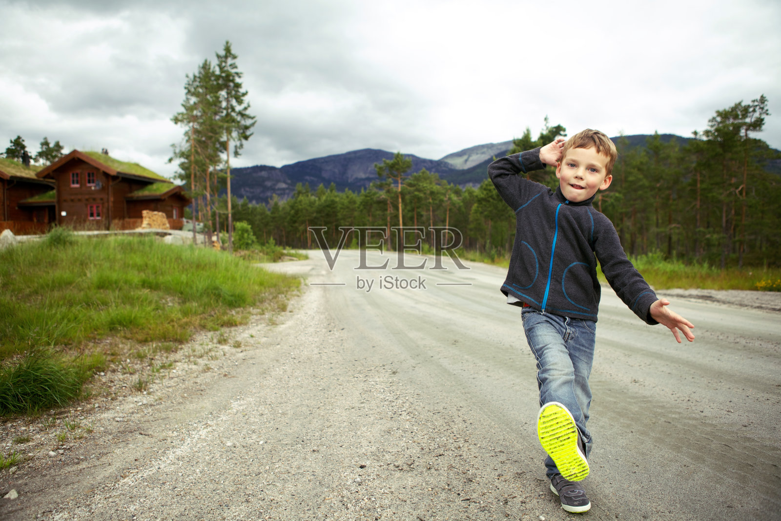 滑稽可爱的小男孩，蹒跚学步的孩子，独自走在挪威的一条土路上，抬起他的脚，露出他的鞋底。照片摄影图片