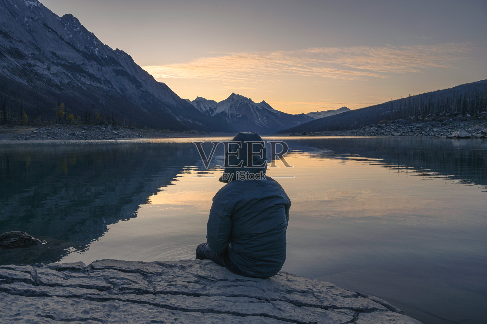 早晨，在贾斯珀国家公园，一名男子坐在梅迪辛湖的岩石上照片摄影图片