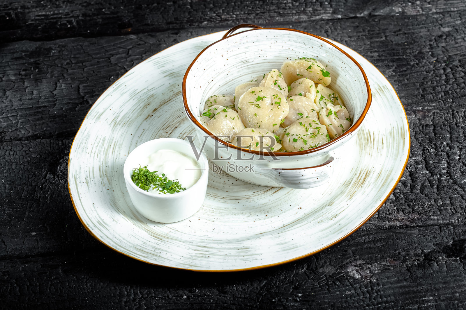 背景是黑烧焦的木头，结构，白色的盘子，自制的香草和酱饺子照片摄影图片