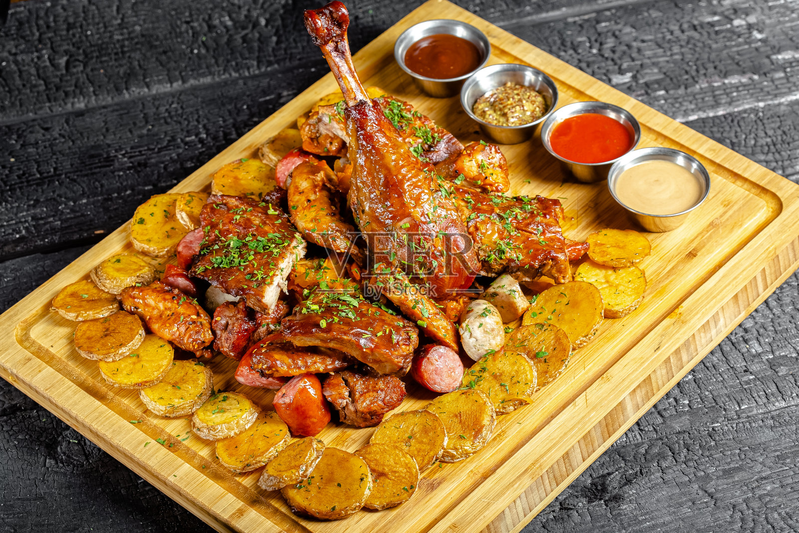 背景是炭黑烧焦的森林，结构，木制砧板，火鸡鸡腿，撒上绿叶的炸土豆，酱汁和碗照片摄影图片