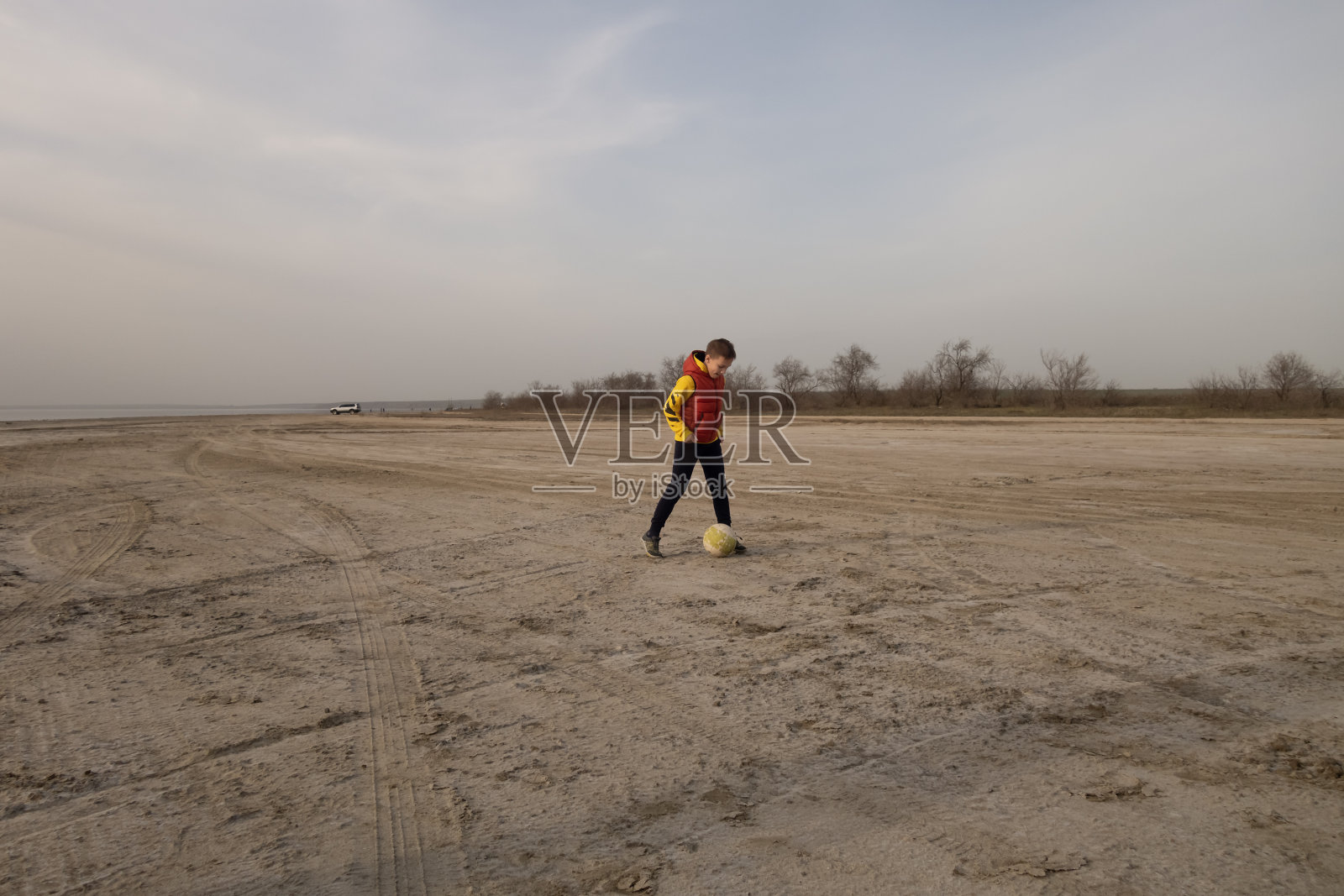 一个10岁的男孩在空旷的沙滩上踢足球。照片摄影图片