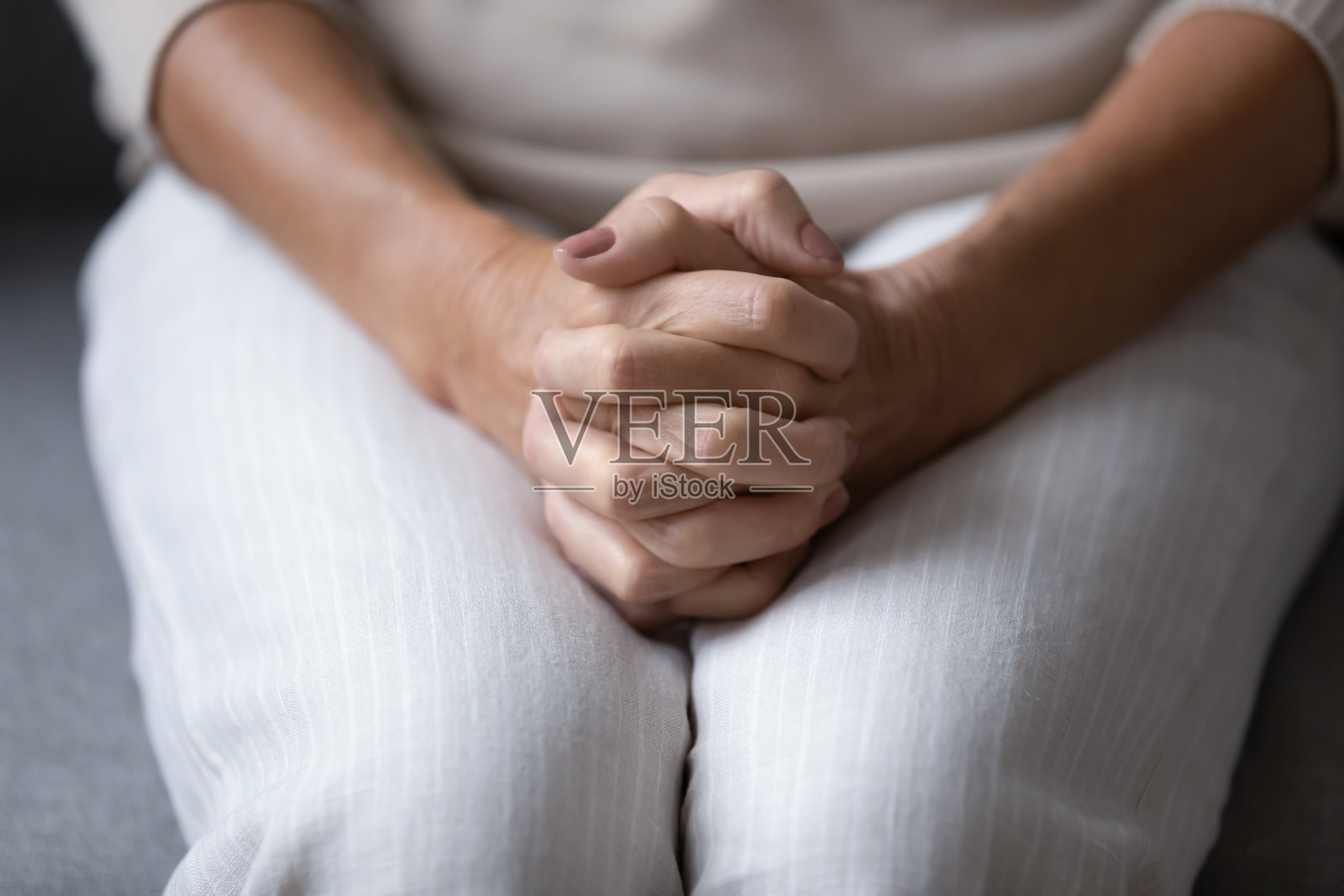 靠近皱巴巴的女人的手在膝上合在一起。照片摄影图片