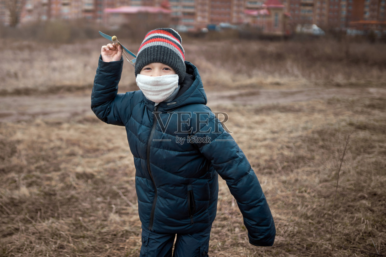 戴着医用口罩的学龄男孩拿着玩具飞机。在城镇附近的空旷地带散步照片摄影图片