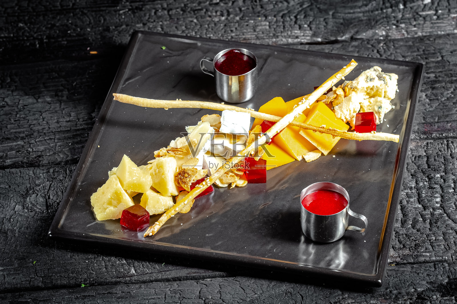 背景黑色烧焦的木头，结构，扁平的黑色方形盘子，小吃酒精，奶酪切割，组合，两种酱料照片摄影图片