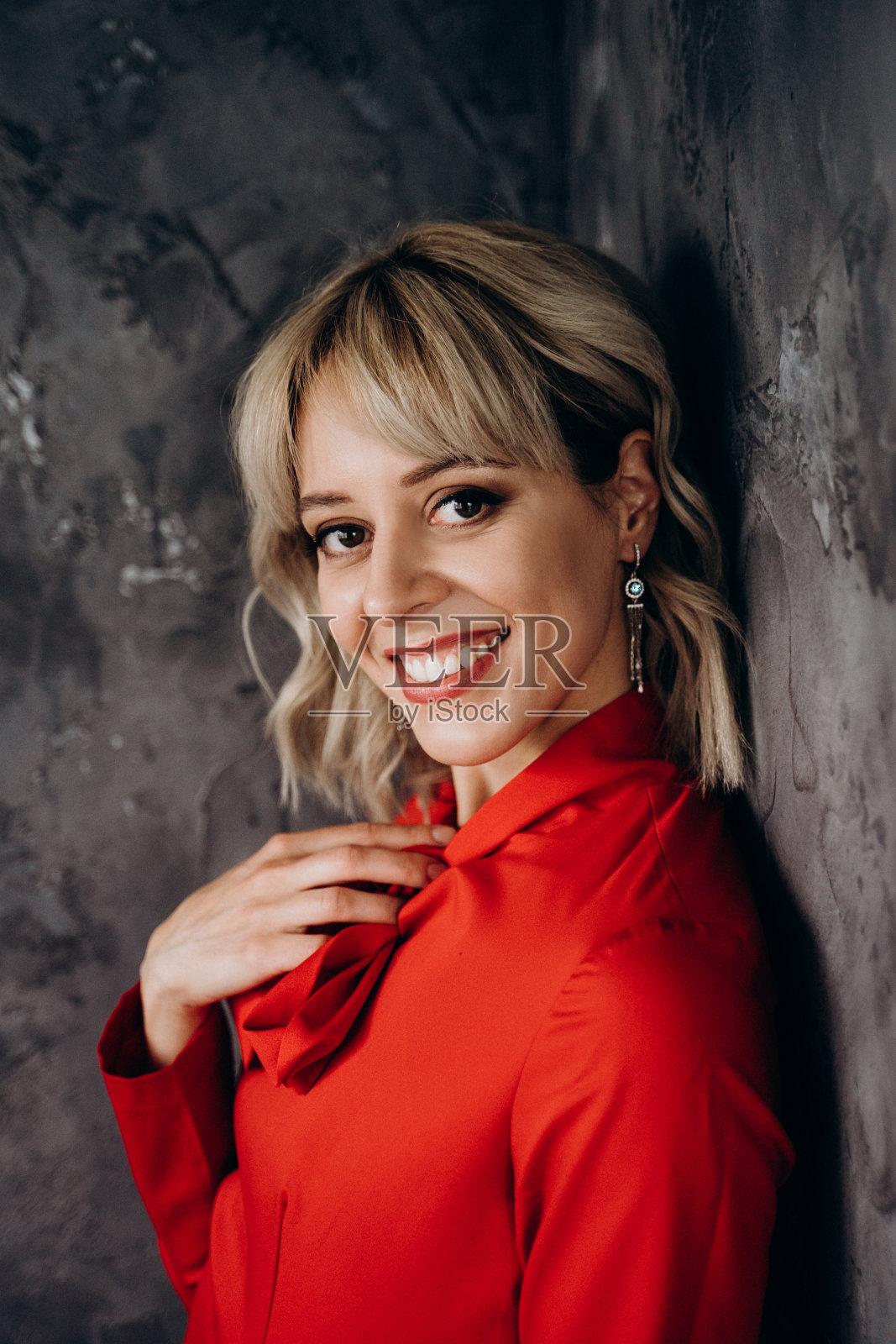 美丽优雅的金发女子在灰色墙壁上拍摄的长袖红色连衣裙照片摄影图片