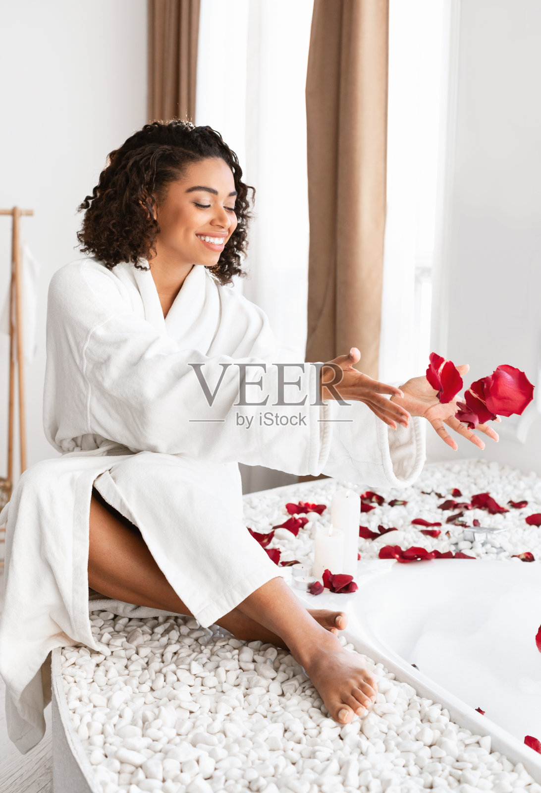 可爱的黑人女孩把玫瑰花瓣扔进泡沫浴缸照片摄影图片