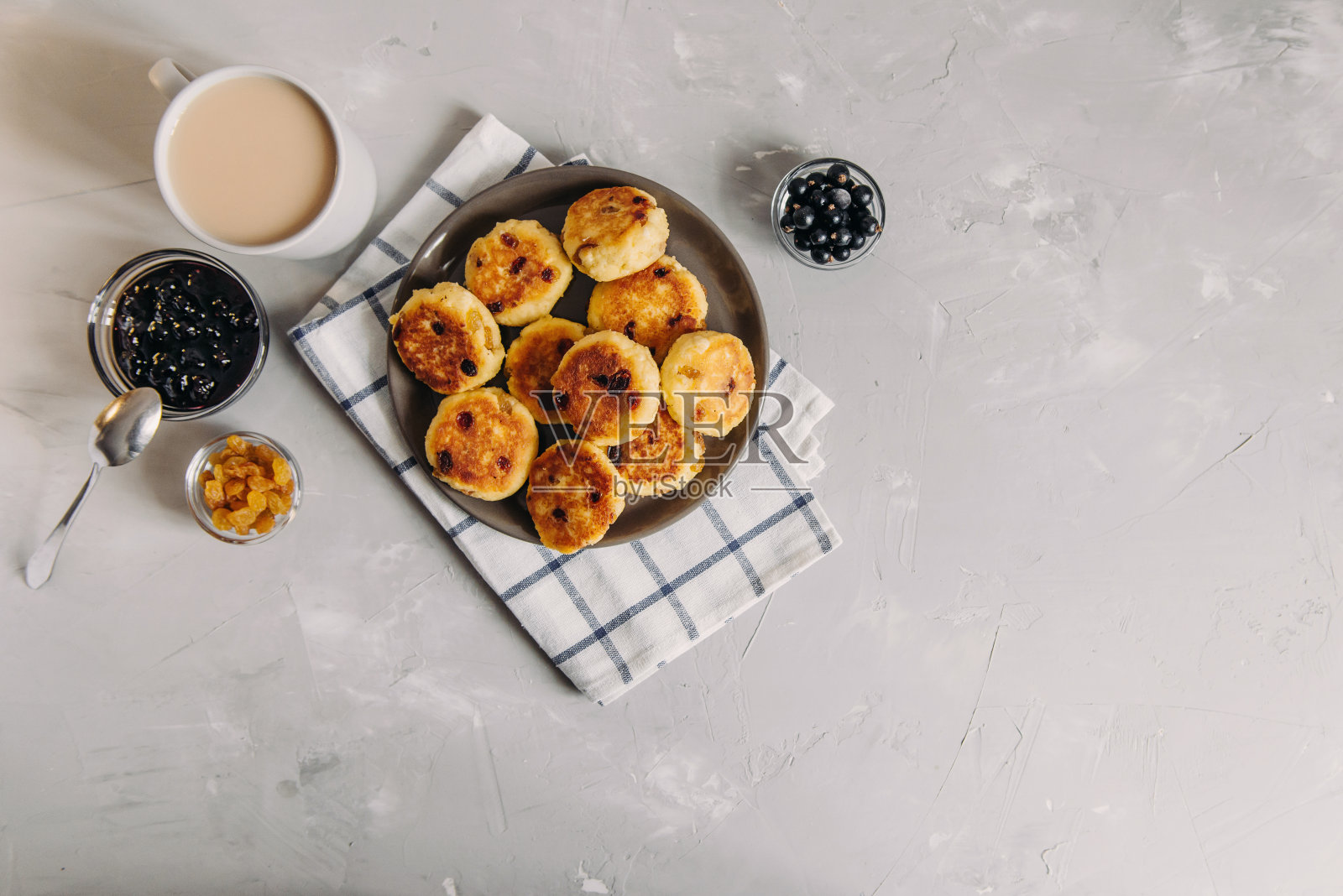 早餐是凝乳煎饼，配茶和果酱。一盘带葡萄干的白干酪，背景很淡。健康食品，快速早餐食谱照片摄影图片