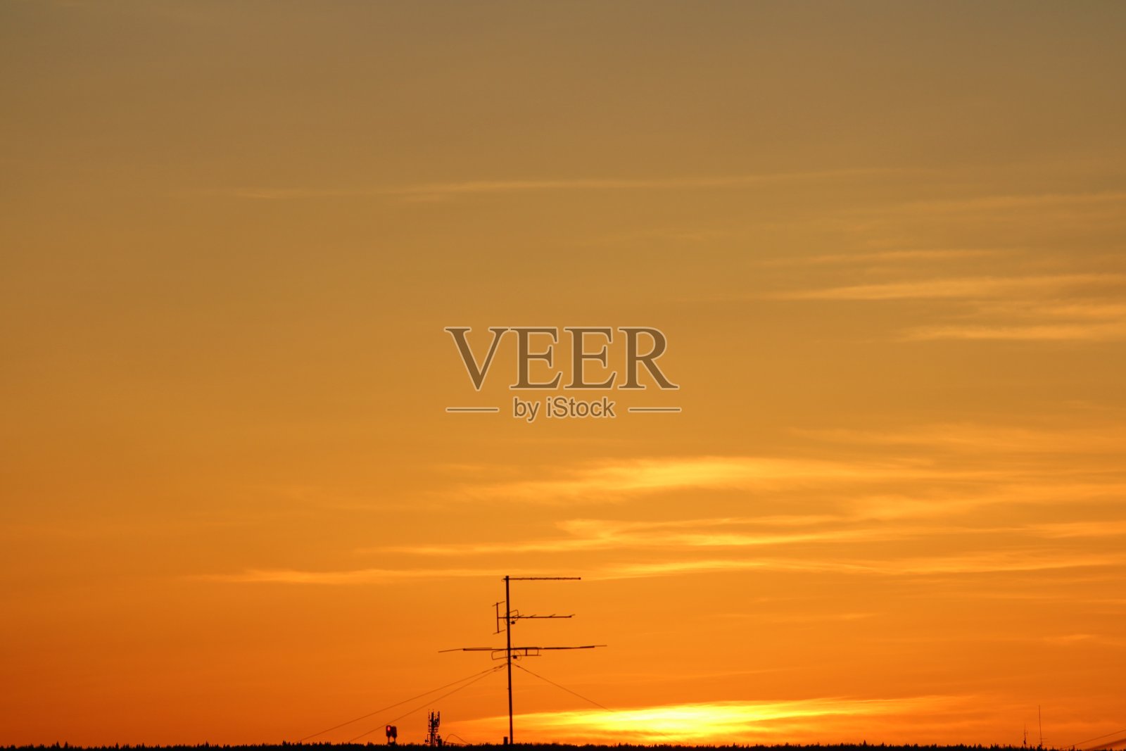 太阳在地平线下，电视天线在背景云在火红戏剧性的橙色天空在日落或黎明由太阳背光。放置文本和设计照片摄影图片