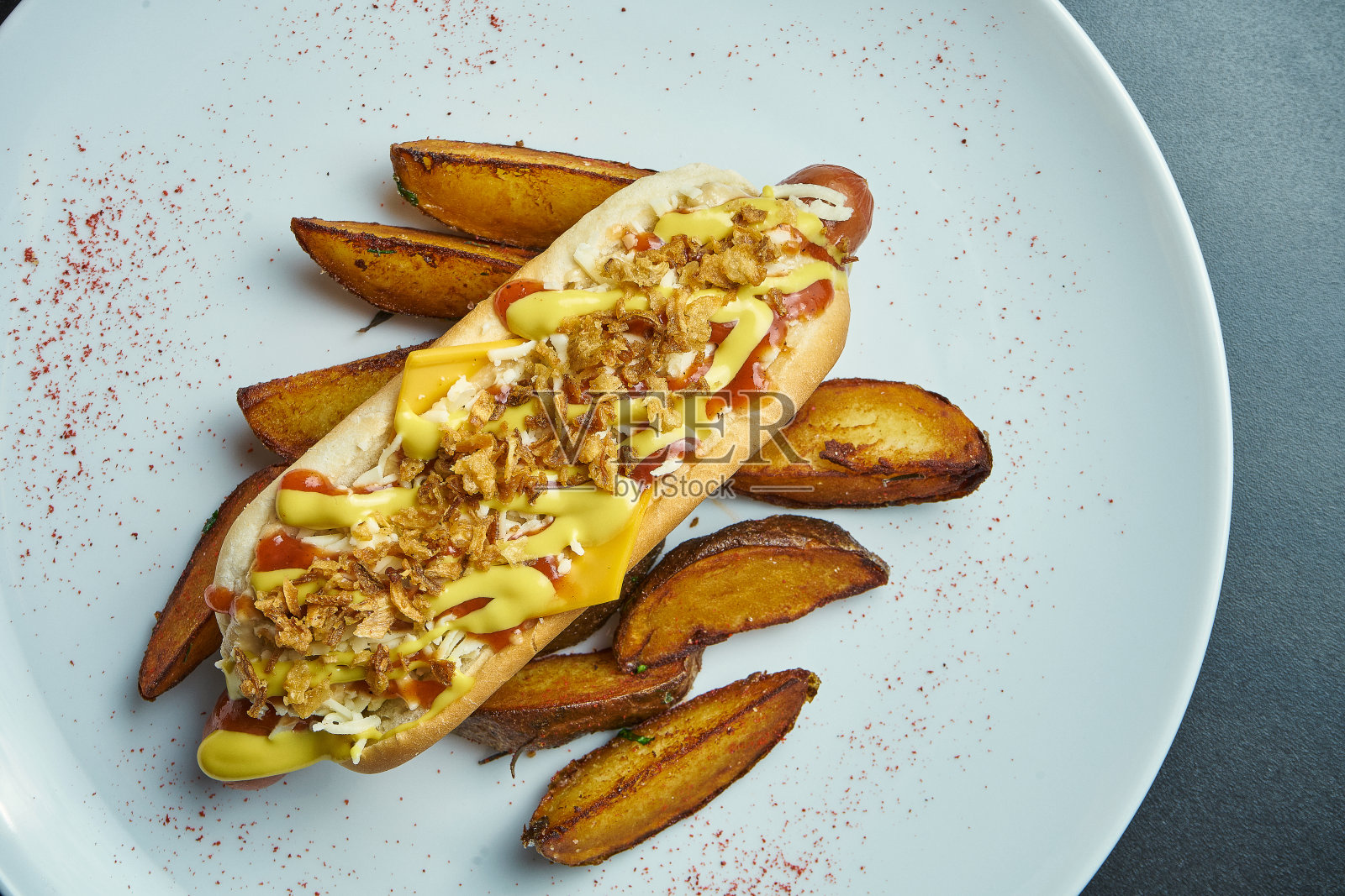 开胃的经典美国热狗，焦糖洋葱，切达奶酪，芥末和番茄酱，配菜土豆在白色的背景。快餐照片摄影图片