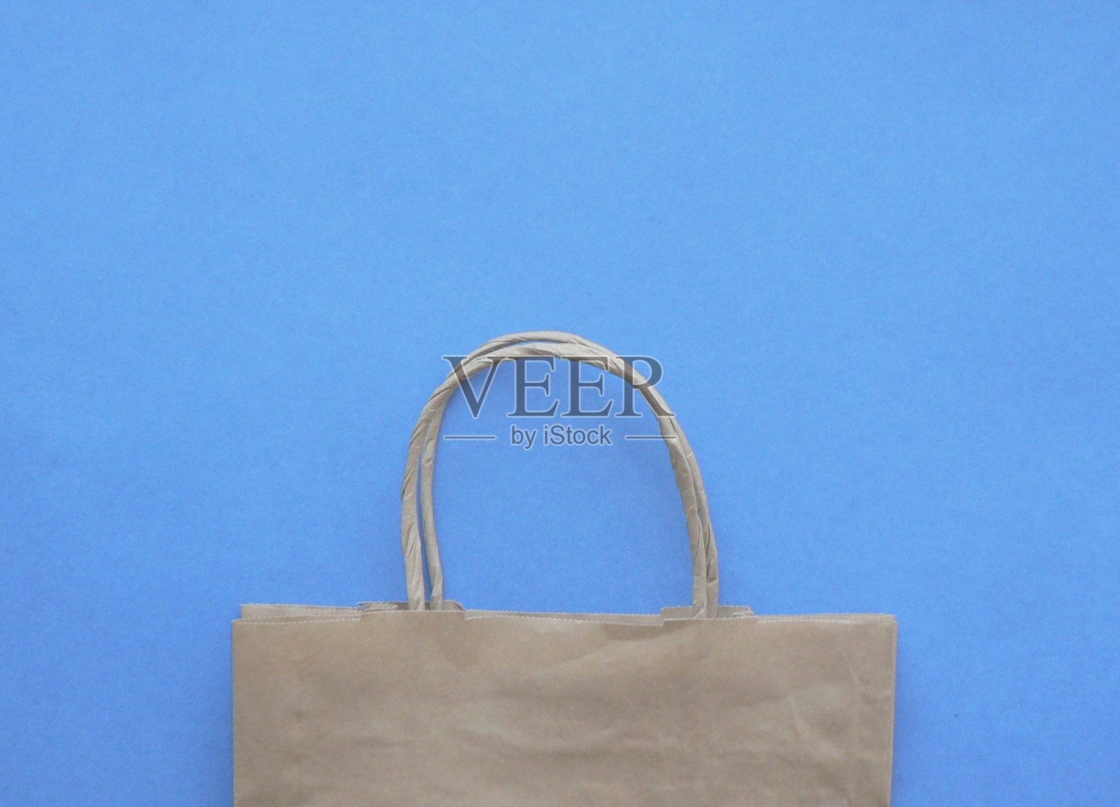 模型的棕色牛皮纸包装与处理，空白工艺购物袋与区域为您的标志或文本，食品交付概念。安全的送货上门。蓝色背景与复制空间。照片摄影图片