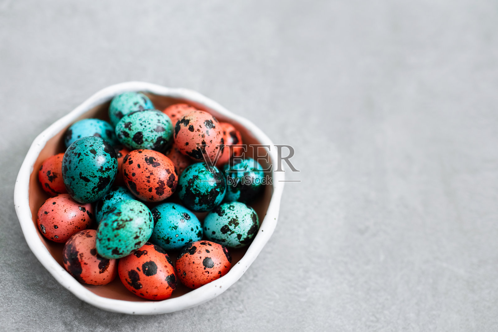 在灰色的混凝土背景上，用小陶瓷板绘成红色和蓝色的复活节鹌鹑蛋。文字和签名的空地方。照片摄影图片