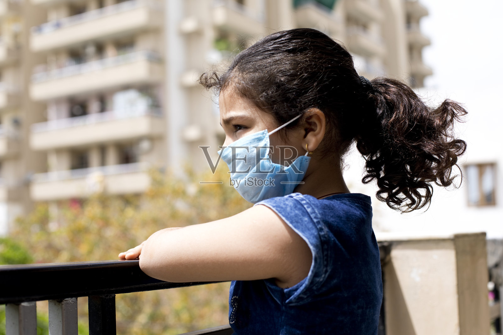 小女孩戴着口罩从阳台往外偷看照片摄影图片