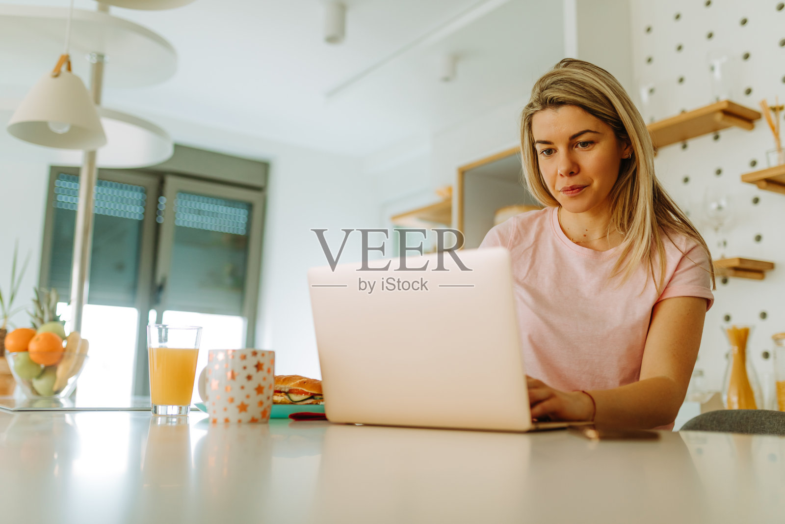 年轻女子坐在厨房里用笔记本电脑看早间新闻。年轻女子担心冠状病毒大流行。照片摄影图片