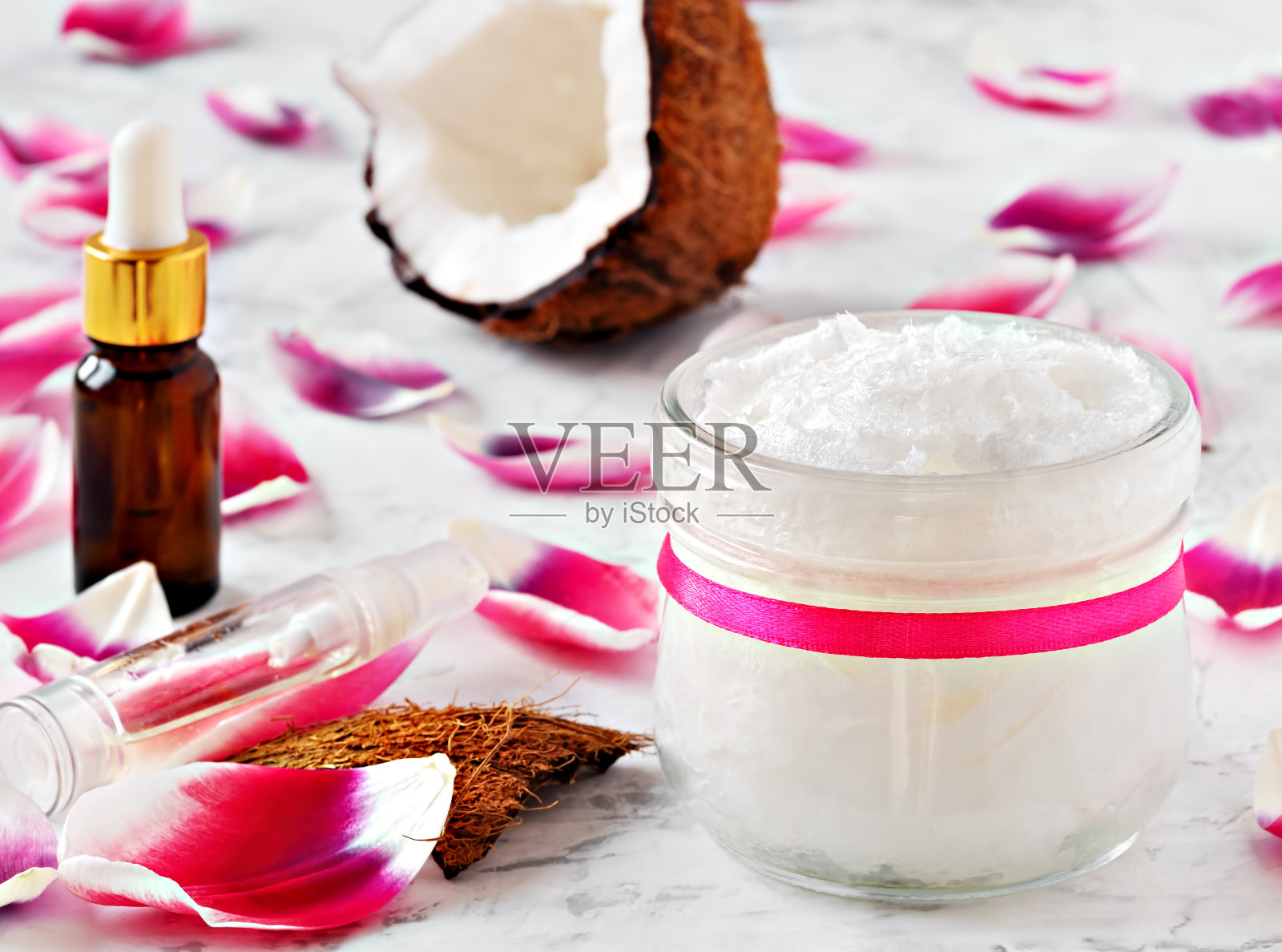 椰子油和替代疗法的椰子在木制的白色背景。桌上有粉红色的花瓣。近距离照片摄影图片