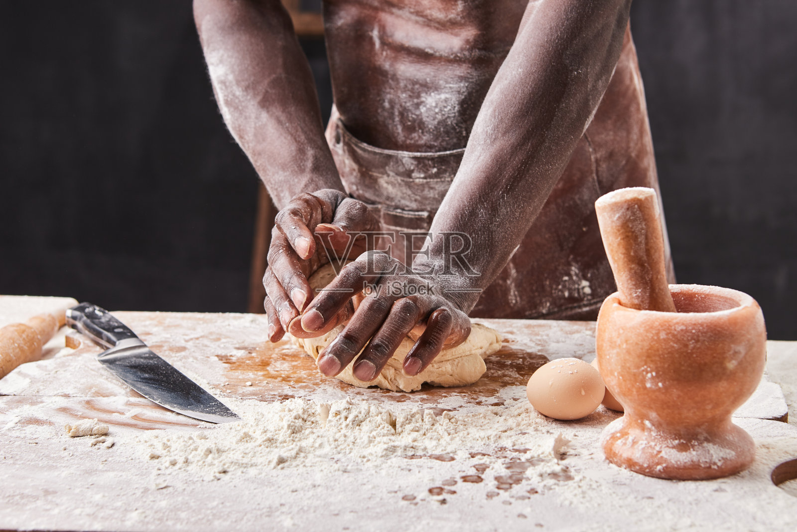 深色皮肤的面包师在厨房揉面团。糕点师为披萨面食准备酵母面团。照片摄影图片