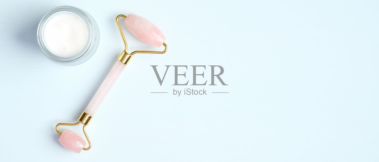 玫瑰石英石辊面部按摩与保湿霜罐在蓝色背景。平铺，俯视图，拷贝空间。玉脸按摩器，护肤理念的美容工具照片摄影图片