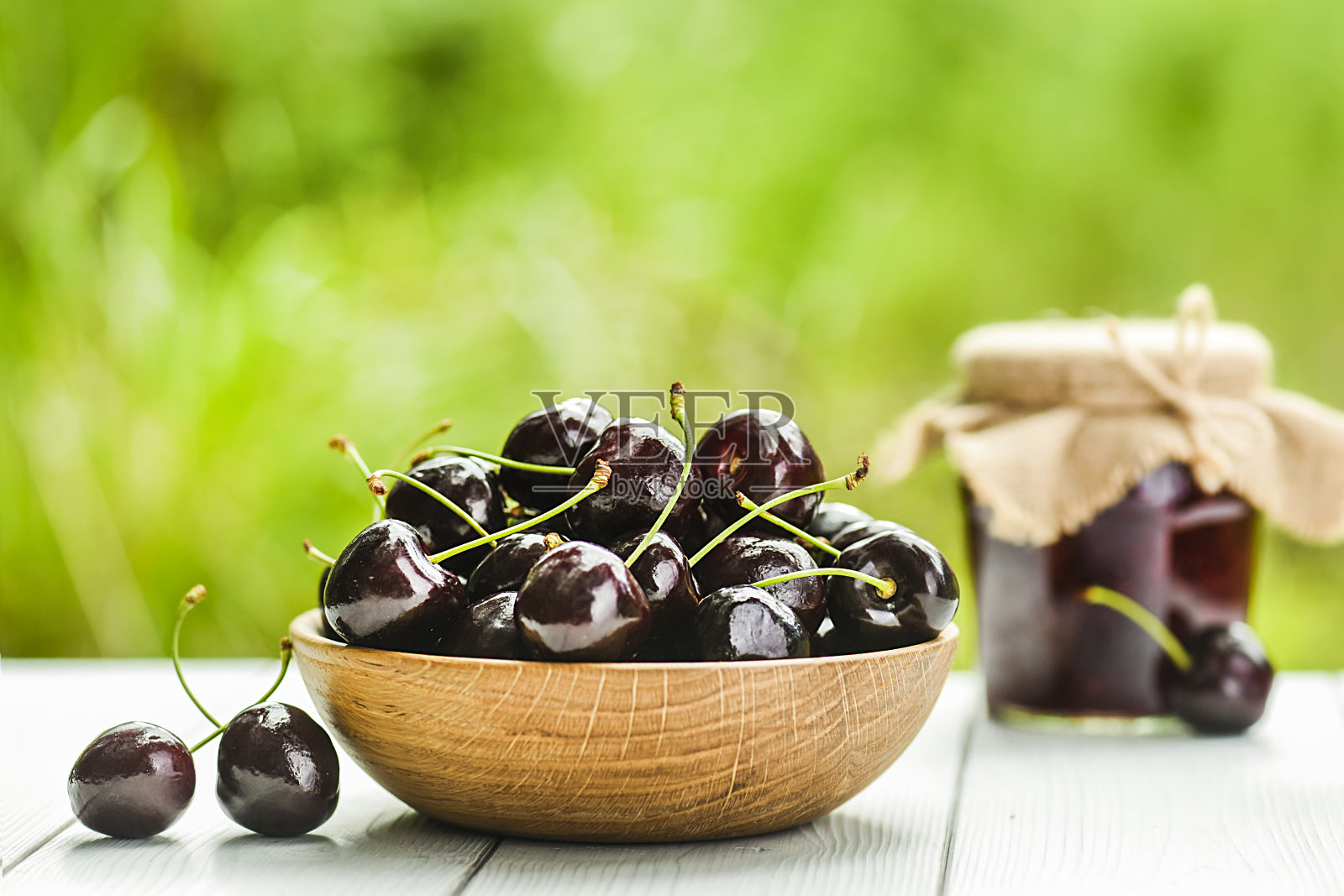 白桌上木碗里的黑樱桃。照片摄影图片