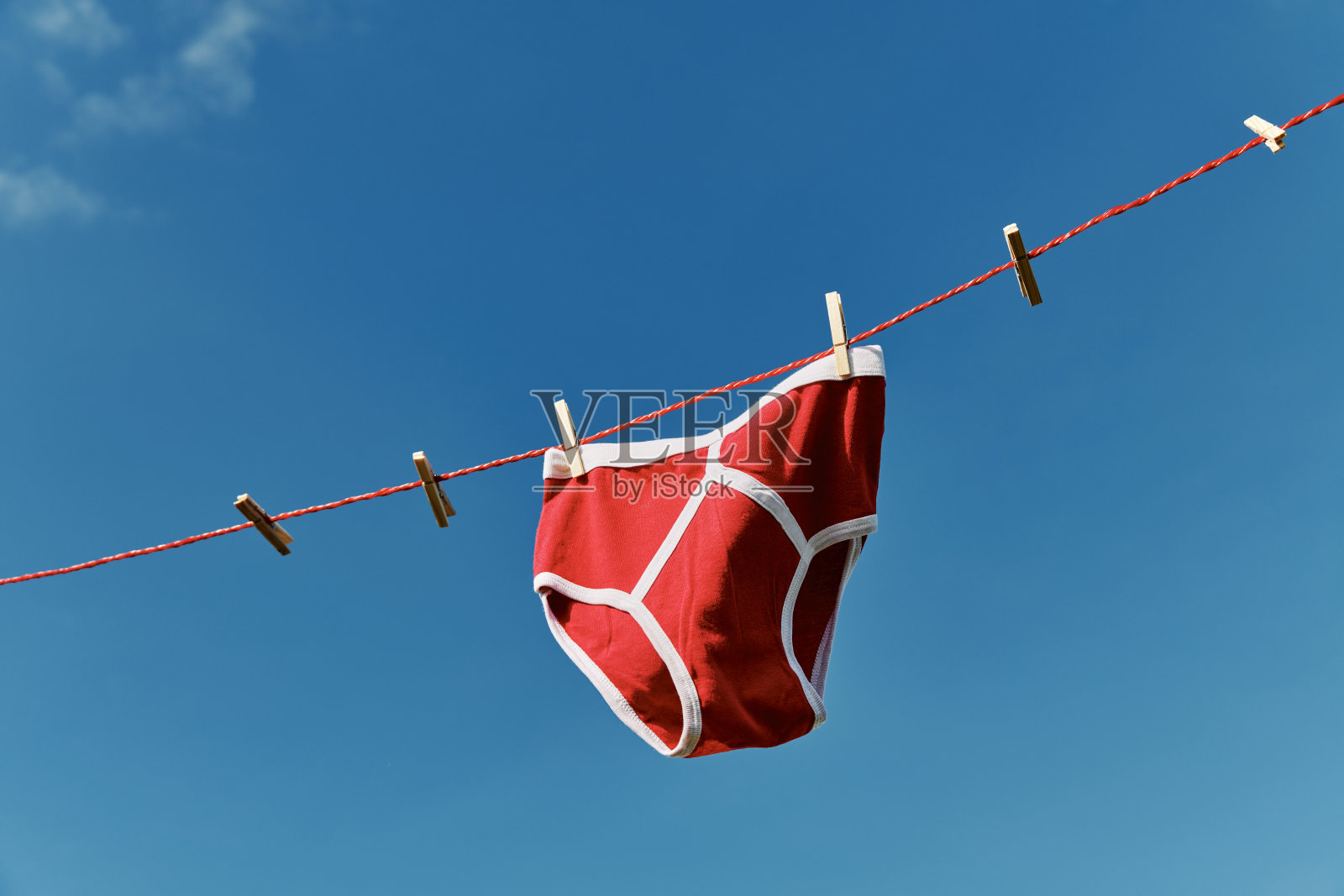 在湛蓝的天空下，晾衣绳上挂着鲜红的y型前内裤。照片摄影图片