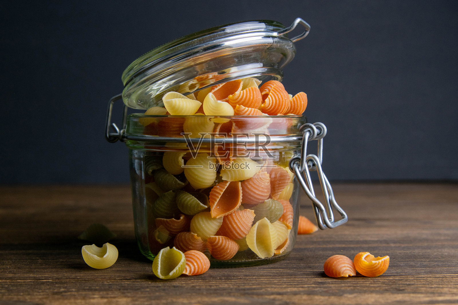 彩色的Conchiglie意面在玻璃罐上的木制背景。正面视图，特写照片摄影图片