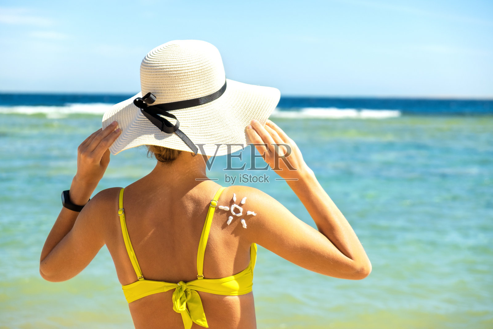 年轻女子在海滩上晒黑与防晒霜在太阳的形状在她的肩膀上。紫外线防晒和防晒护肤概念照片摄影图片