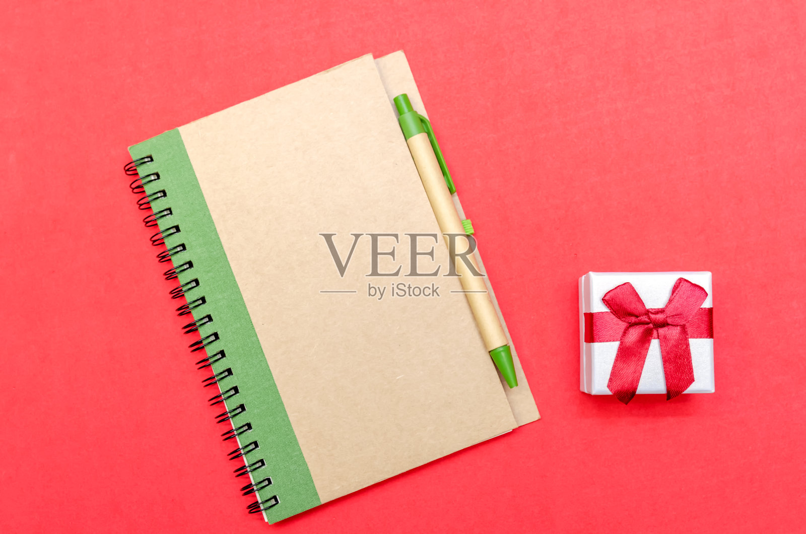 带钢笔的记事本和红色背景的礼物。平面位置，俯视图。节日的概念，情人节，圣诞节，新年照片摄影图片