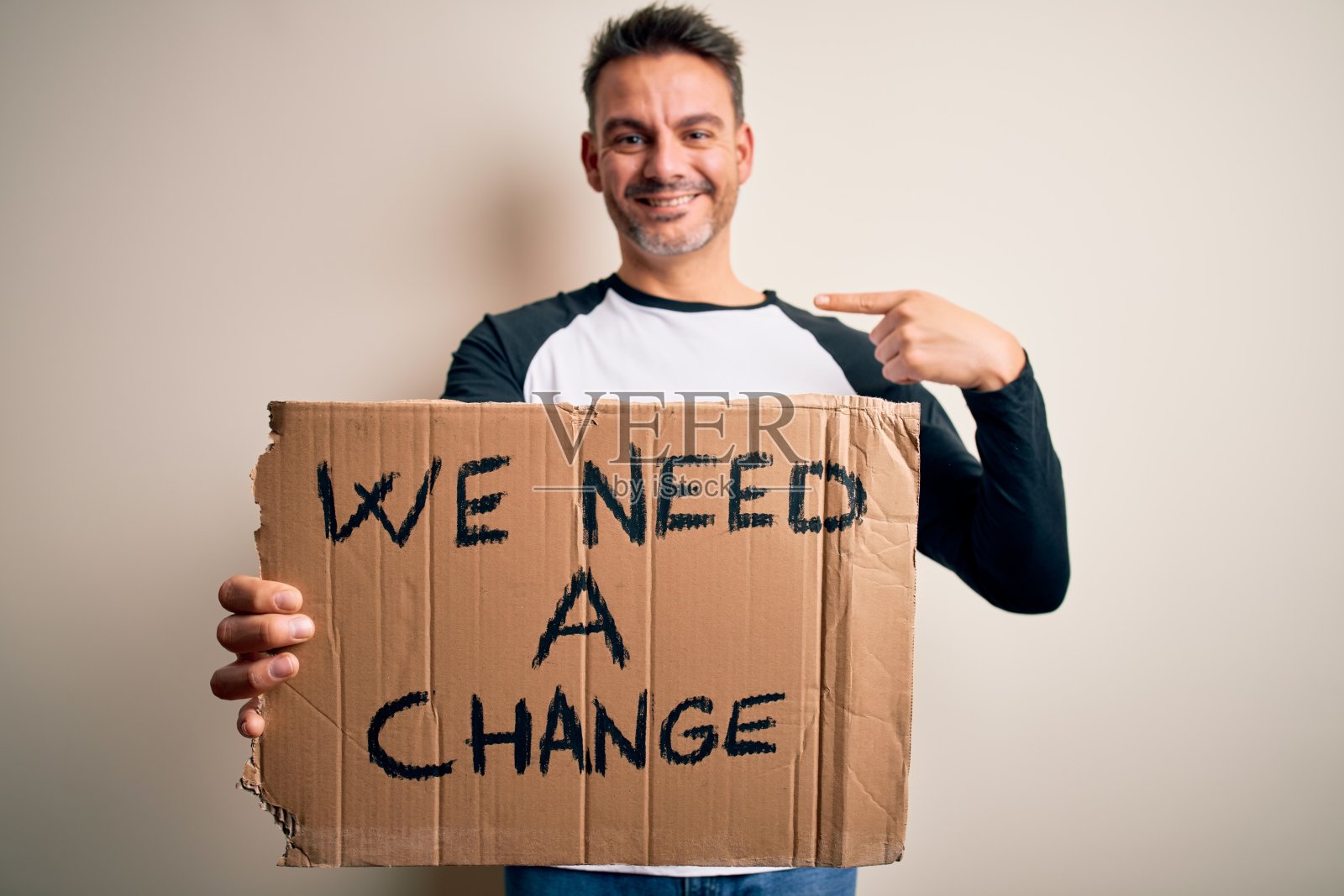 年轻英俊的激进分子男子举着旗帜与改变信息在粉红色的背景与惊讶的脸指向自己照片摄影图片