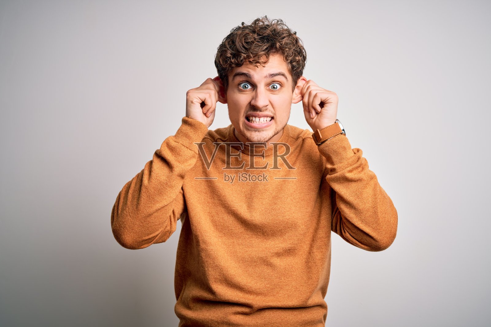 年轻的金发帅哥卷发穿休闲毛衣白色背景微笑拉耳朵用手指，有趣的手势。面试问题照片摄影图片