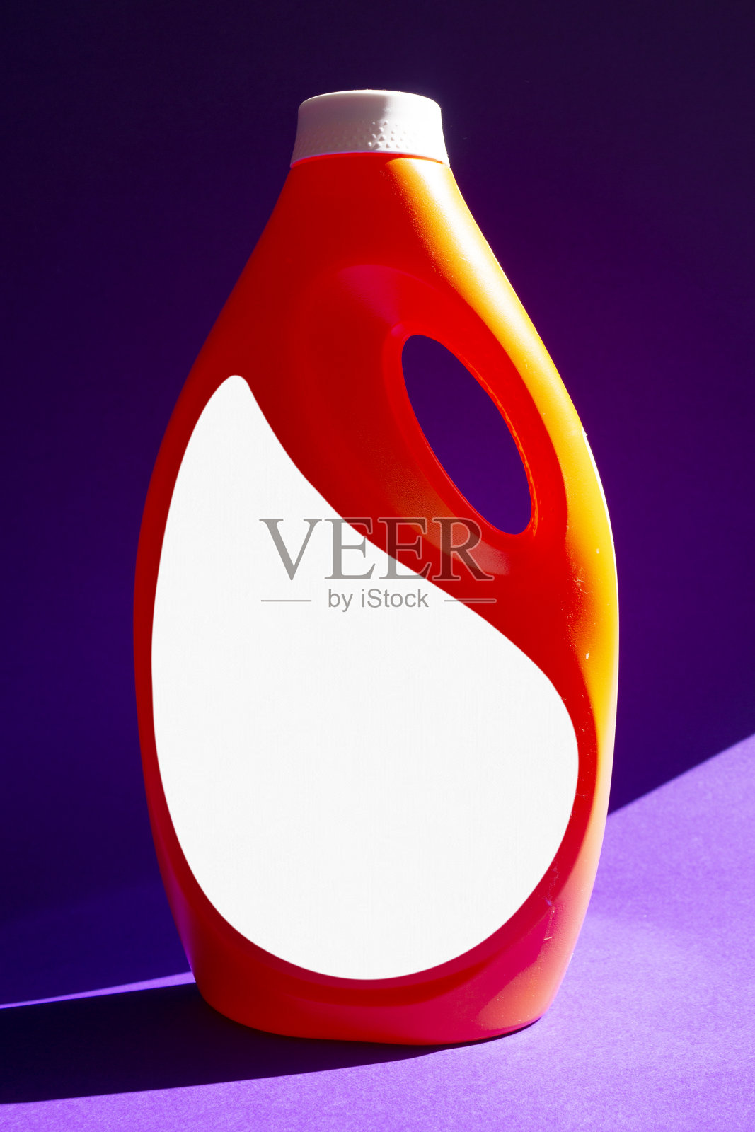 红色的洗涤剂瓶在紫色的纸背景。照片摄影图片