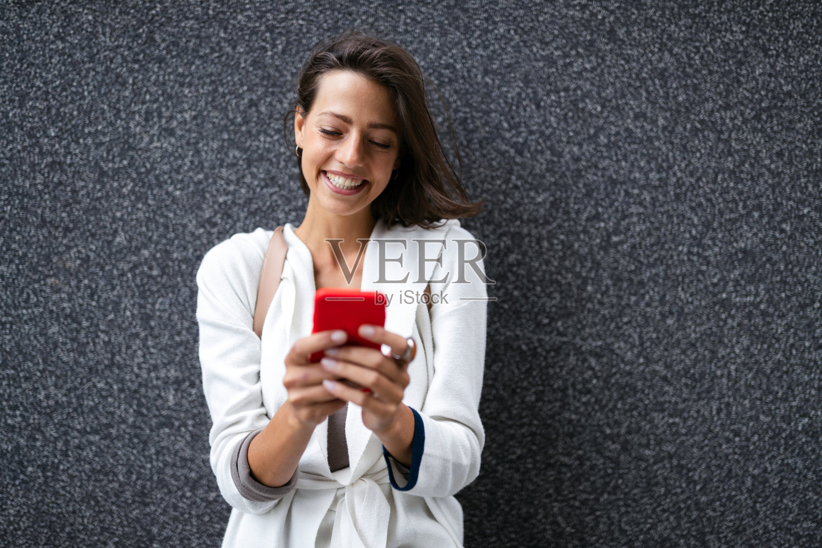 美丽的年轻快乐的女人拿着智能手机在城市的街道上照片摄影图片