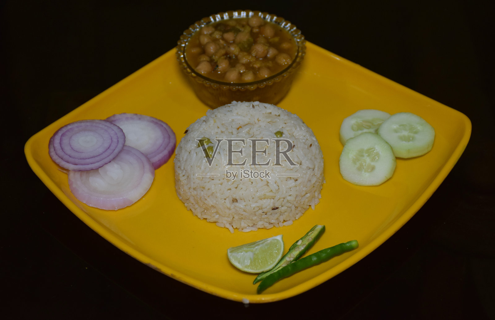 美味的印度菜Chawal Chole(鹰嘴豆饭)和切好的洋葱，黄瓜，柠檬和青椒放在一个黄色的盘子上，孤立在黑色的背景照片摄影图片