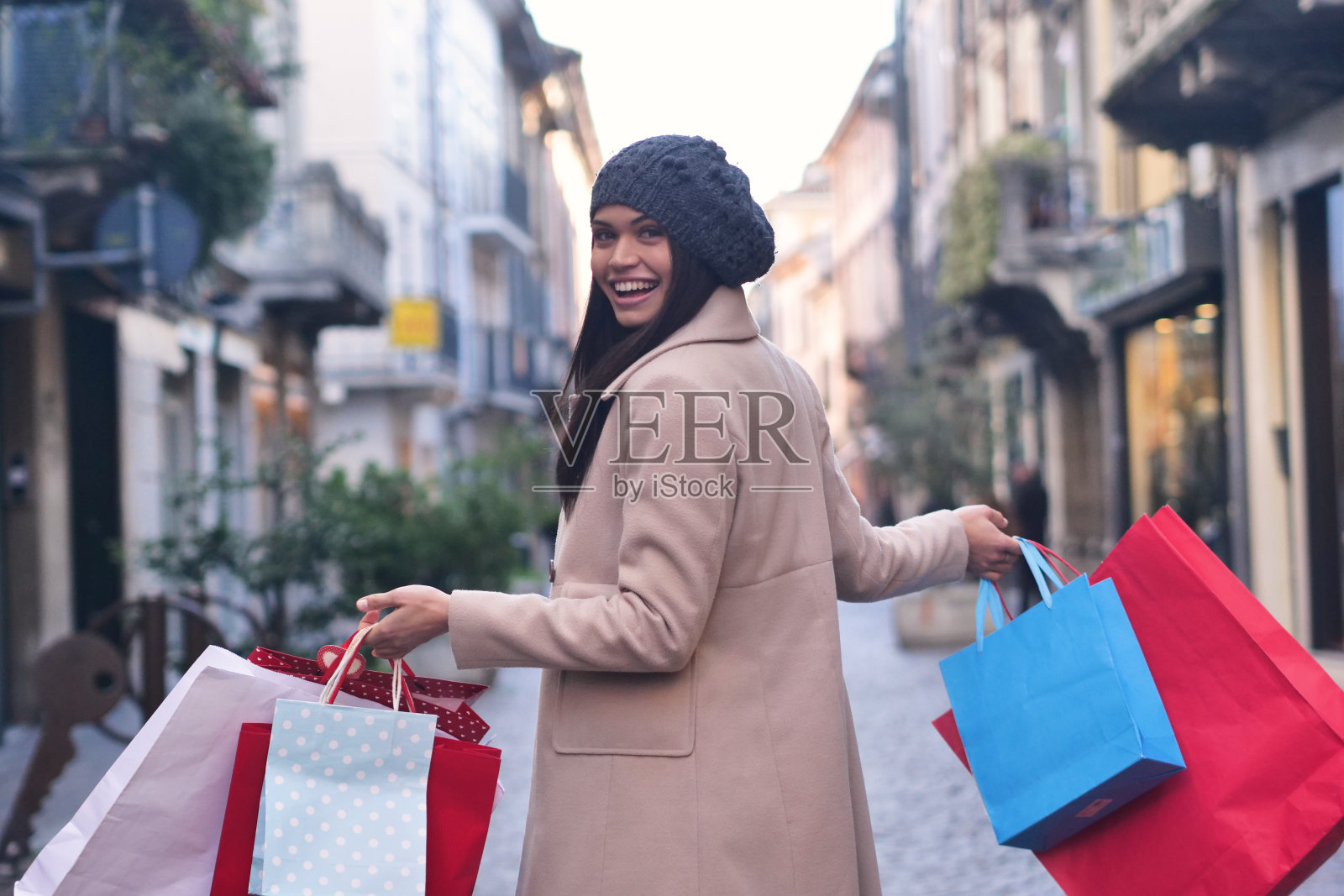 一个年轻漂亮的女孩在市里的商店购物时喜欢购物。这个女孩拿着许多五颜六色的手提包。照片摄影图片
