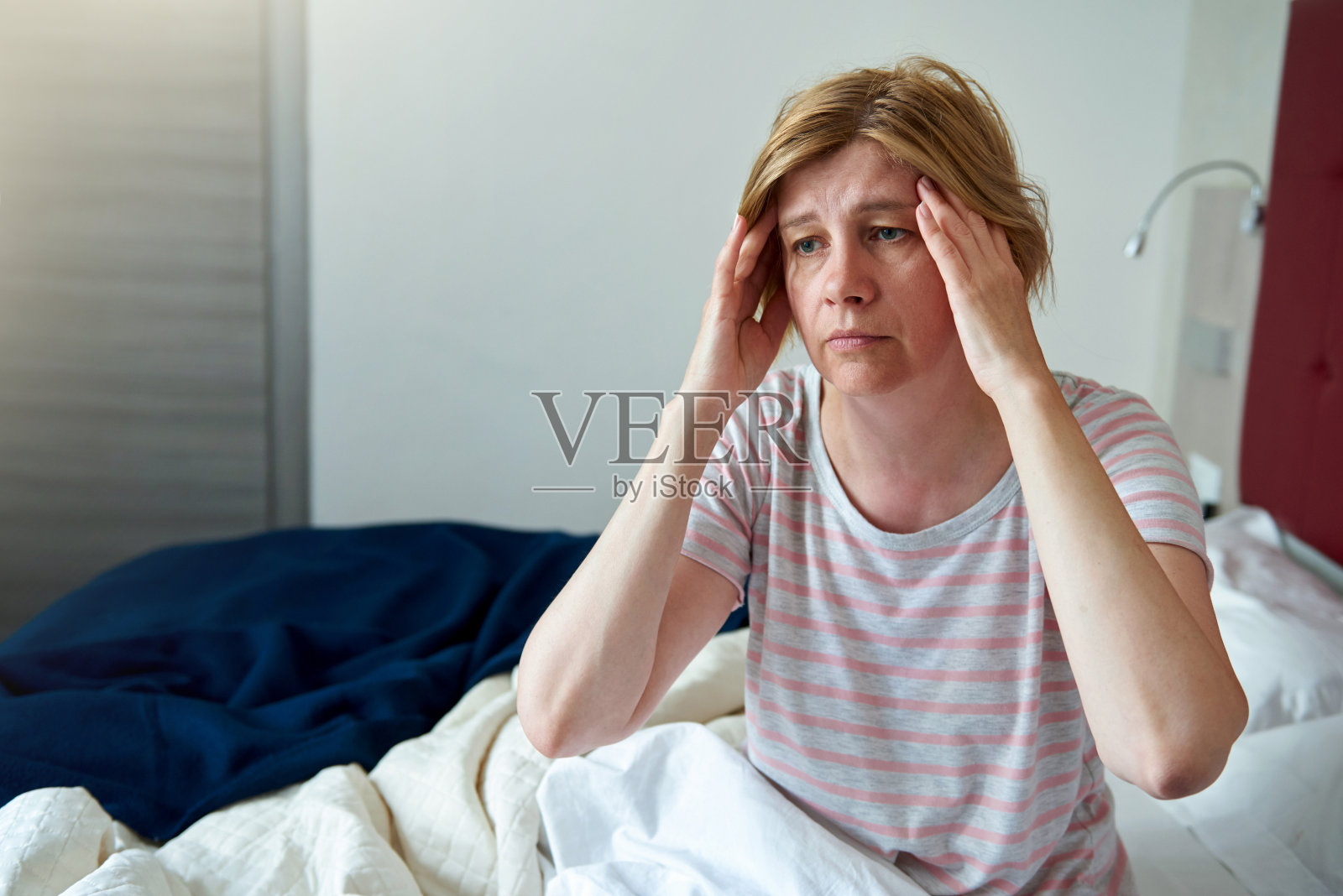 头痛的女人。一位中年妇女抱着头坐在床上。照片摄影图片